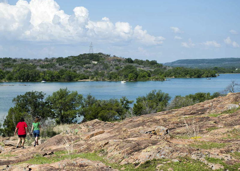 two people walking on rocky ground near river