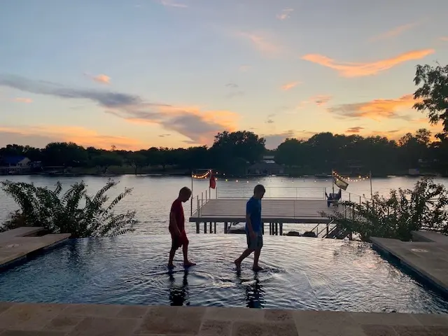 two people walking across a pool at sunset