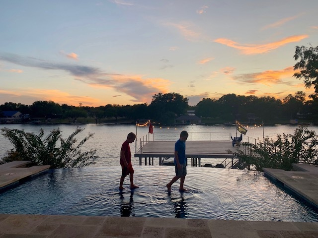 two people walking across a pool at sunset